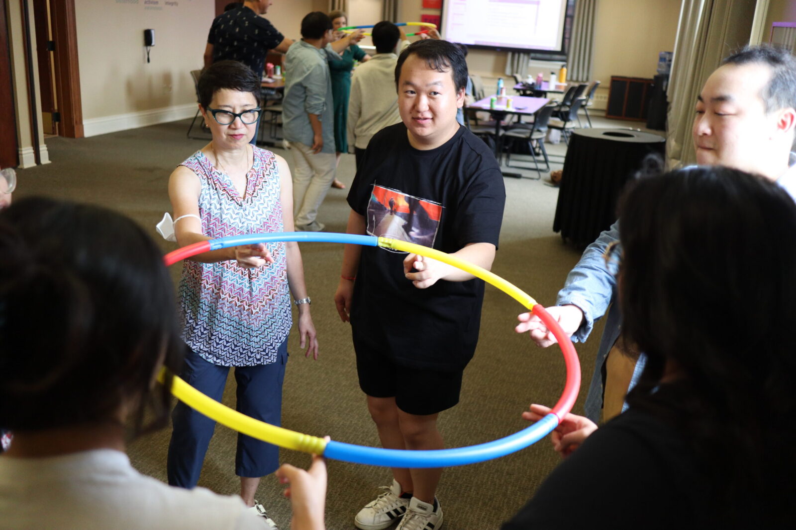 A group of people standing in a circle who are all holding the same hula hoop together.